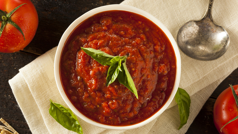 A bowl of marinara sauce alongside fresh basil and garlic