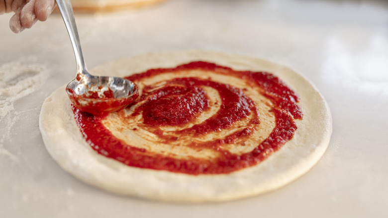 Hand adding pizza sauce to pizza dough with spoon