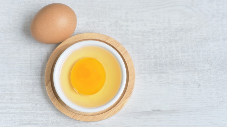 cracked egg in bowl next to whole egg