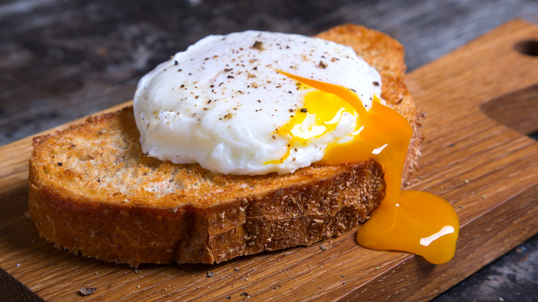 A poached egg on toast on top of a wooden cutting board