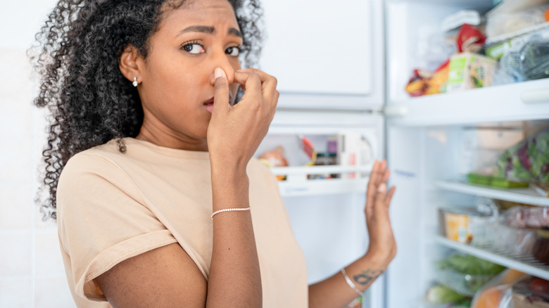 Woman smelling unclean refrigerator full of food