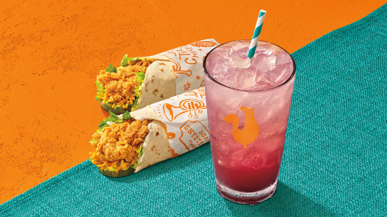 Two of Popeyes' new Chicken Wraps and a glass of its new Blueberry Lemonade sit on a turquoise cloth against an orange background
