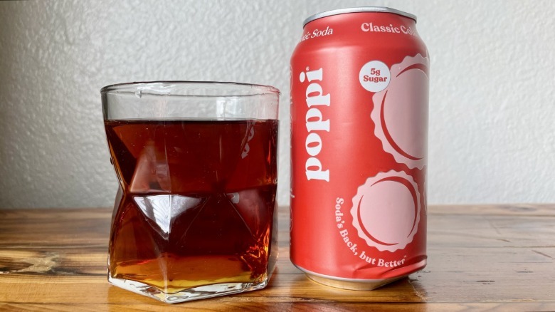 Glass and can of Poppi Classic Cola on a wooden table