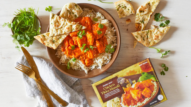A Chicken Tikka Masala frozen dinner box sits next to a bowl of prepared food garnished with herbs and naan bread