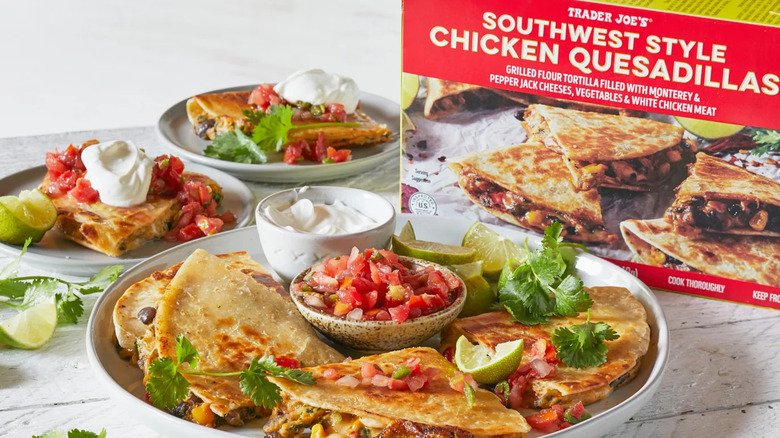Plates of prepared Southwest Style Chicken Quesadillas with salsa, sour cream, lime wedges, and cilantro sit near the product package