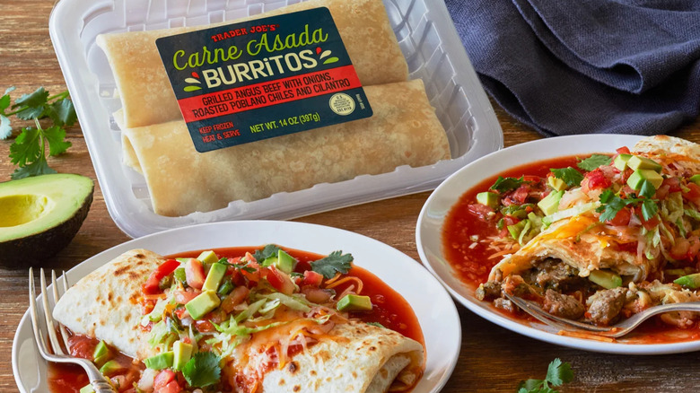 A pack of Trader Joe's Carne Asada Burritos sits near two plates with prepared burritos covered in sauce and toppings