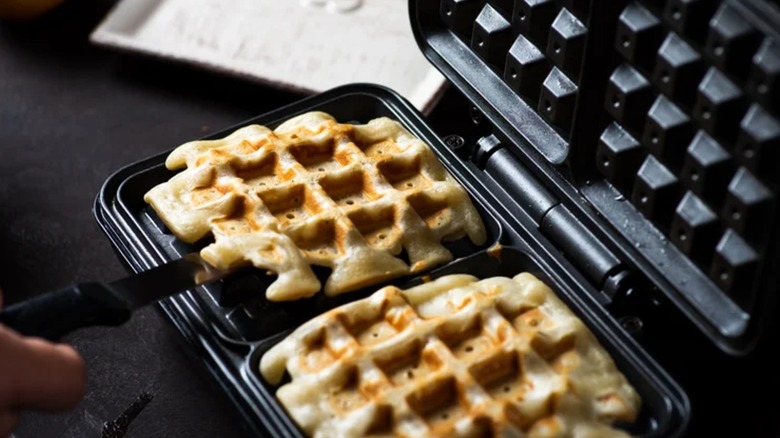 Two waffles in a press iron being scooped out by the cook
