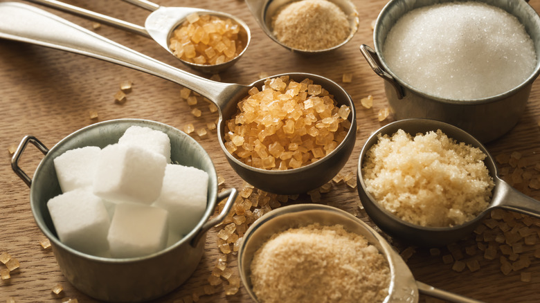 Various types of sugars in metal spoons and bowls.