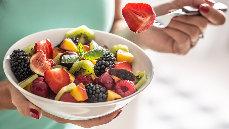 Person holding a bowl of chopped fruit.