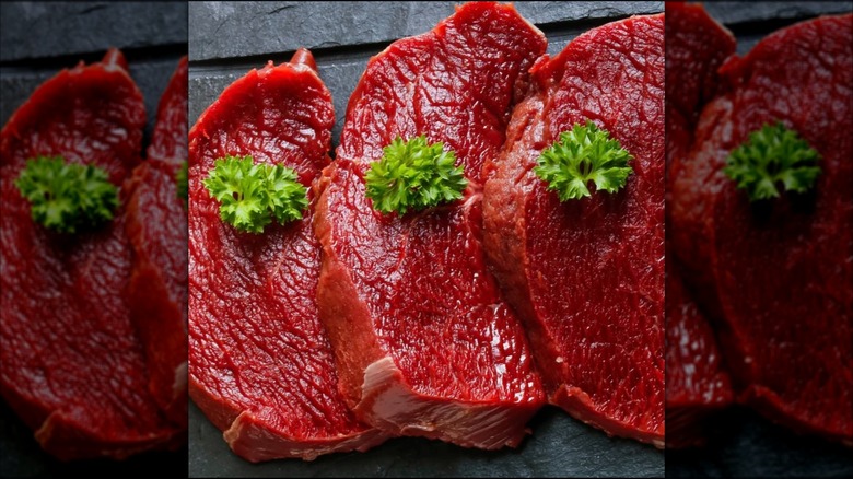 Trio of raw elk steaks on a stone surface with garnishes