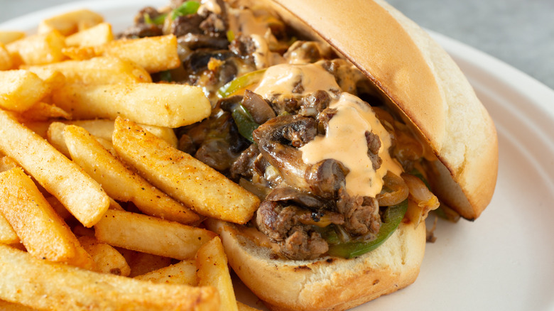 A Philly cheesesteak close up next to fries