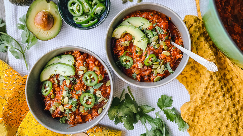 Pumpkin and turkey chili in bowls on table with garnish