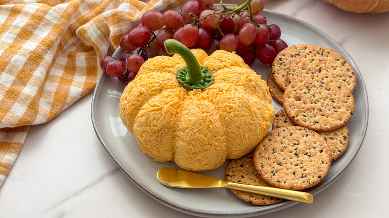 pumpkin cheese ball on plate with crackers and grapes