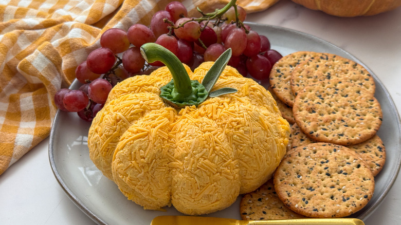 Pumpkin cheese ball on plate with crackers and grapes