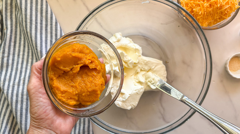 hand adding pumpkin to bowl with cream cheese