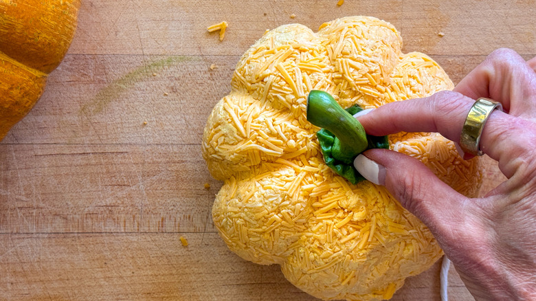 Hand pressing pepper stem into pumpkin cheese ball