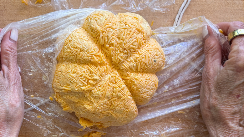 hands removing plastic wrap from pumpkin cheese ball