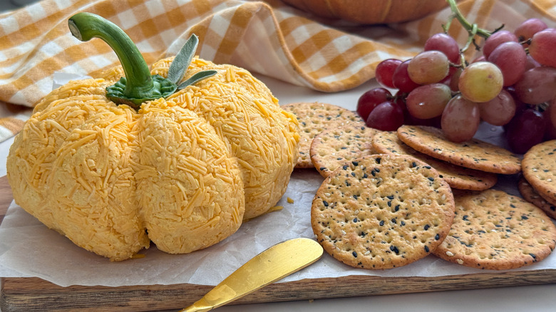 Pumpkin cheese ball on board with crackers and grapes