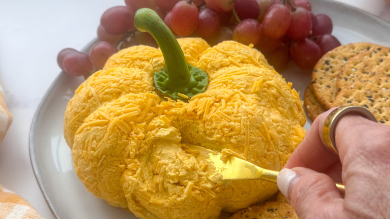 Hand using knife to get serving from pumpkin cheese ball