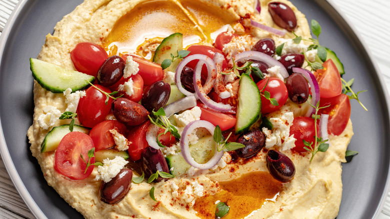 Hummus topped with Greek salad ingredients on a plate