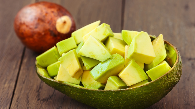 Diced avocado cubes inside of avocado peel with pit in background