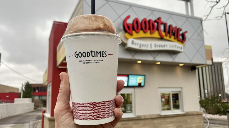Hand holding Good Times Chocolate Milkshake in front of storefront