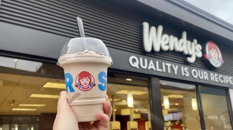 Hand holding Wendy's Chocolate Frosty in front of storefront
