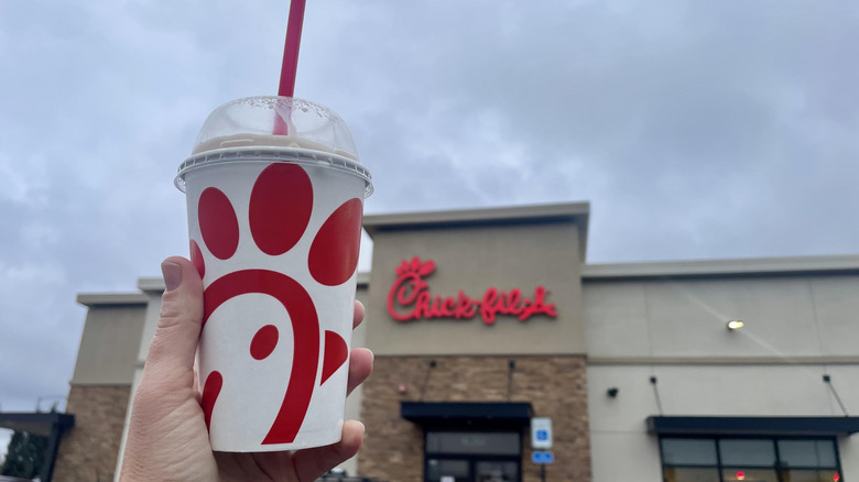 Hand holding Chick-fil-A Chocolate Milkshake in front of storefront