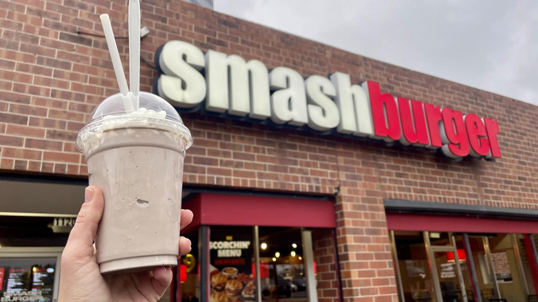 Hand holding Smashburger Chocolate Milkshake in front of storefront