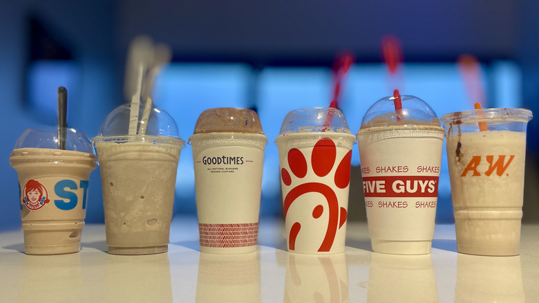 Lineup of six different fast food milkshakes on a white counter