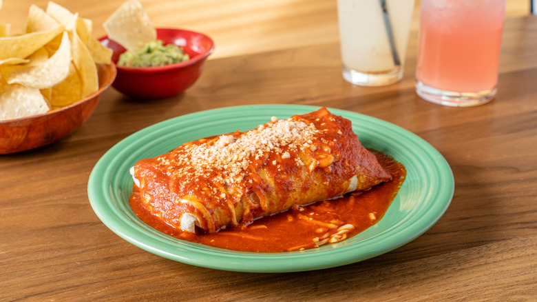 A blue plate has a wet burrito with red sauce and cheese, looking very like an Enchirito