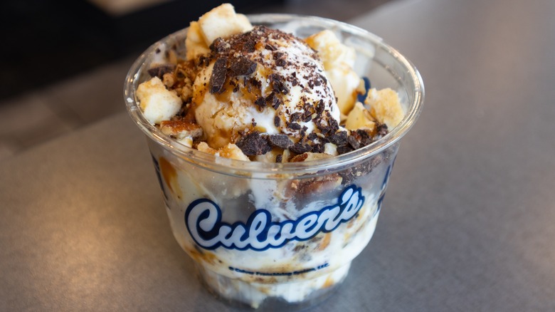 A Culver's frozen custard sundae with vanilla custard, pecans, and a chocolate crumble topping sits on a countertop