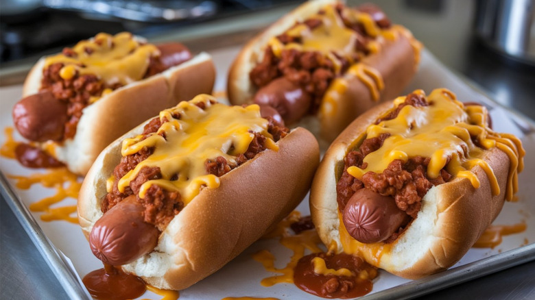 Four chili cheese dogs sit on a lined baking sheet