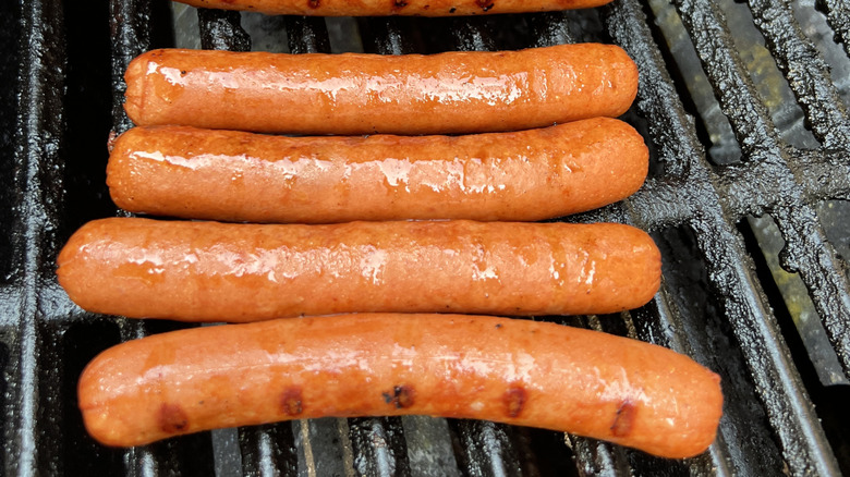 Four hot dogs rest on a grill, getting char marks