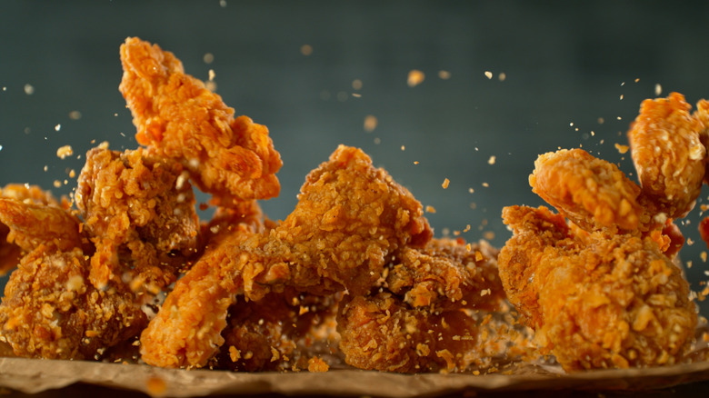 Closeup of fried chicken pieces with breading crumbs flying through the air around them