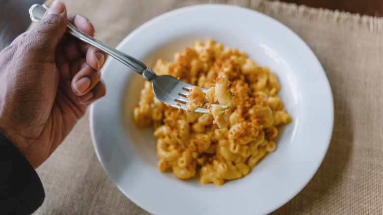 A person holds a forkful of creamy mac and cheese over a bowl.