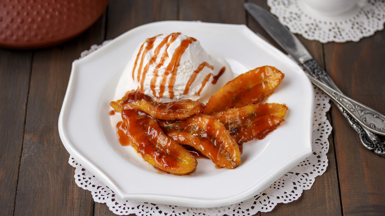 a plate of bananas foster with a scoop of vanilla ice cream rests on a country table