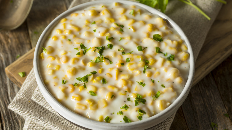 a bowl of creamy corn is topped with fresh herbs