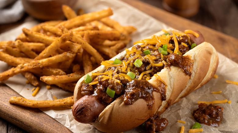 A chili cheese dog next to some seasoned french fries.