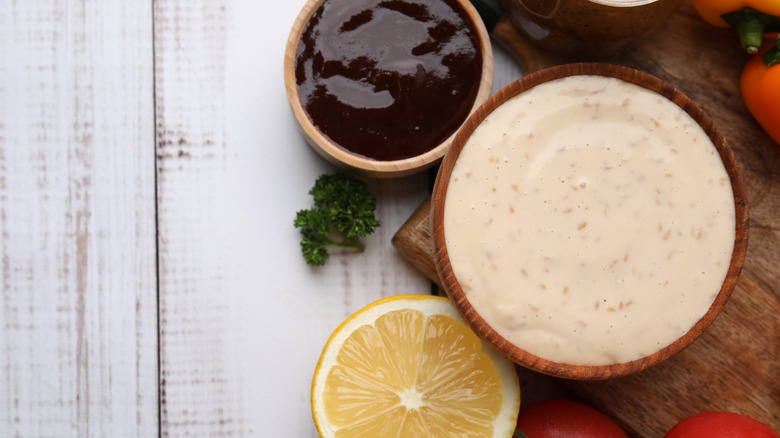 A small bowl of Baltimore Tiger barbecue sauce sits on a wooden board beside a thick brown sauce and a lemon half