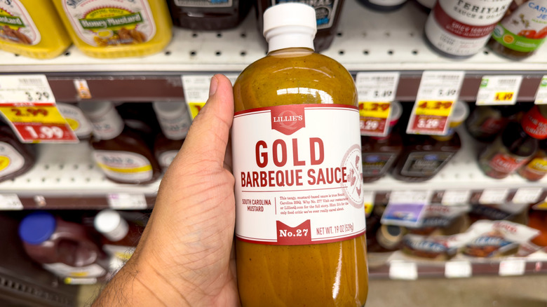 A person holds a bottle of Carolina Gold barbecue sauce in a grocery store aisle