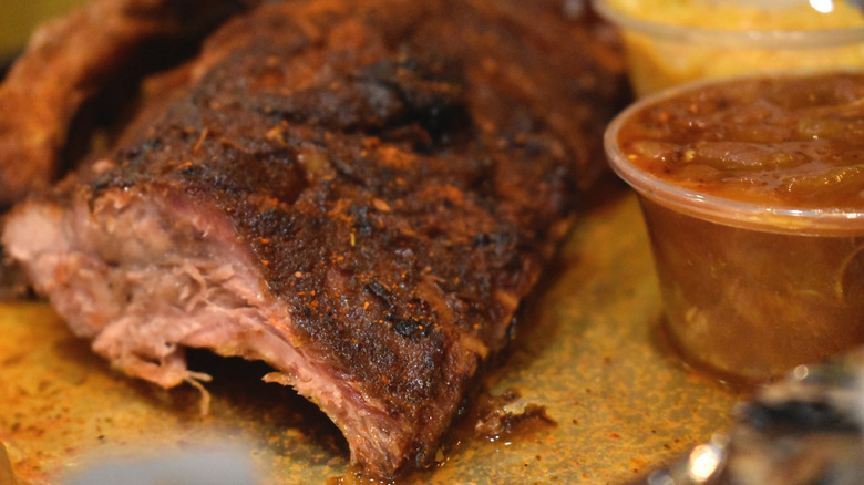 Memphis-style ribs sit on a plate next to a container of Memphis barbecue sauce