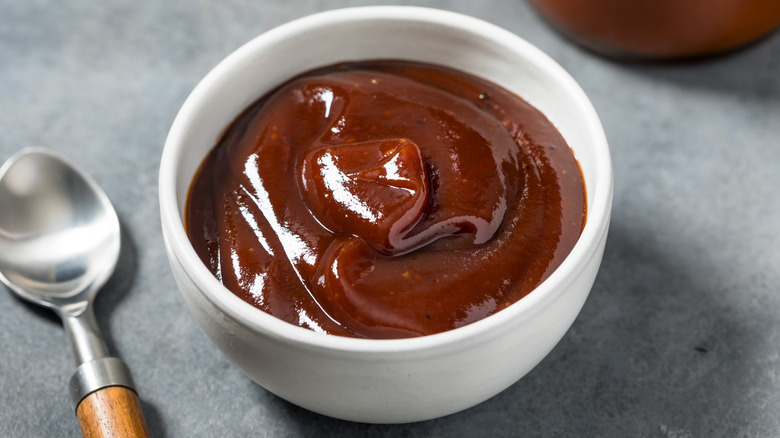 Deeply red Nashville barbecue sauce sits in a white bowl beside a spoon