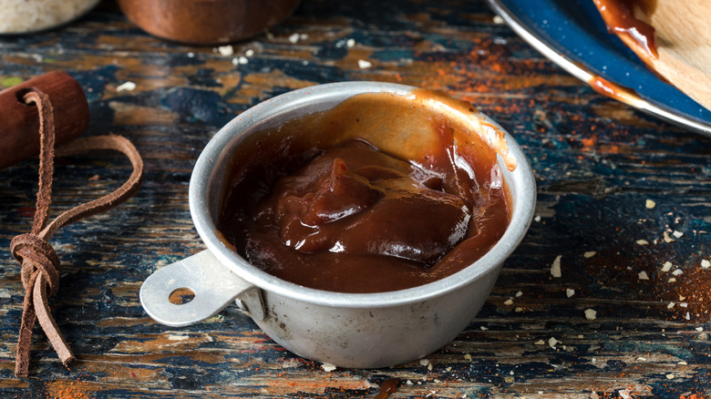 Oklahoma barbecue sauce rests in a metal measuring cup on a wooden table