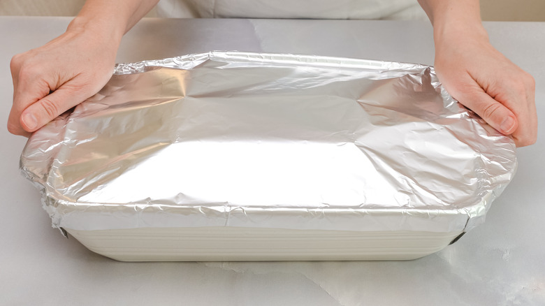 hands holding baking dish covered in foil