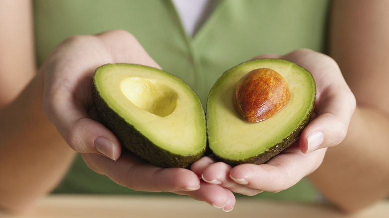 Two hands holding ripe avocado halves