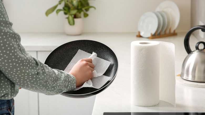 A person wipes down a pan with a paper towel