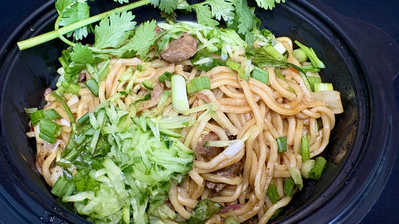 bowl of steak ramen with green vegetables on black background