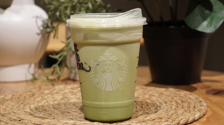 Iced Banana Cream Protein Matcha on a woven placemat in front of plants