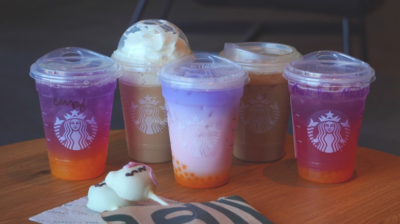Starbucks' Tropical Butterfly Refresher, Horchata Frappuccino, Butterfly Drink, Iced Horchata Shaken Espresso, and Tropical Butterfly Lemonade Refresher (left to right) behind two Unicorn Cake Pops.